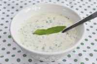 DSC_1241 • nogetiovnen.dk Creamy cucumber yogurt sauce with dill in a white bowl, topped with a green leaf and a spoon.